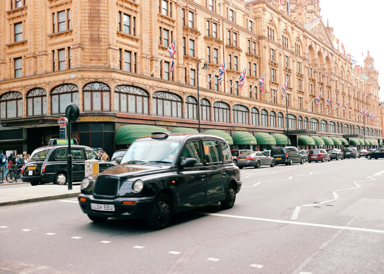 Harrods building in London with black taxi driving by