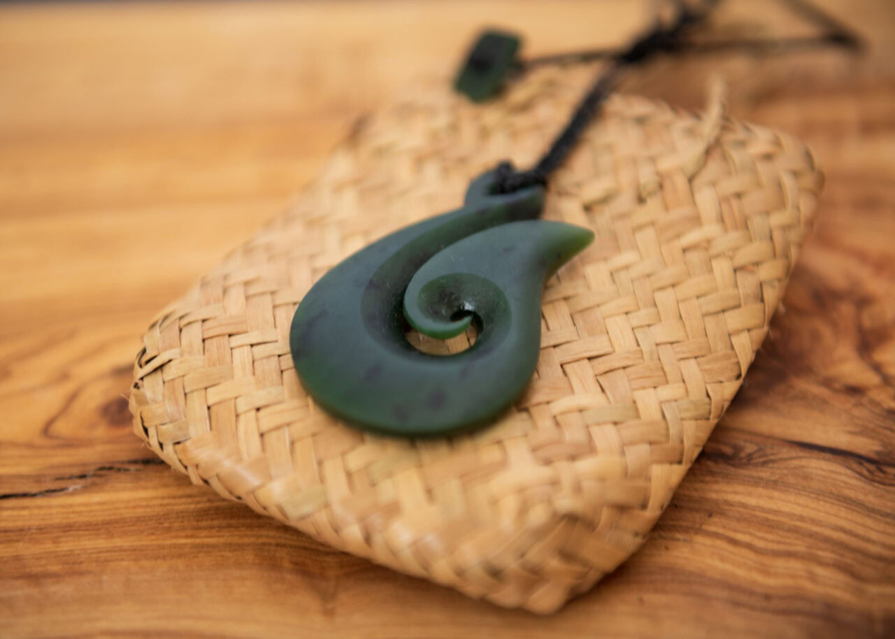 Pounamu fish hook necklace on wooden background.