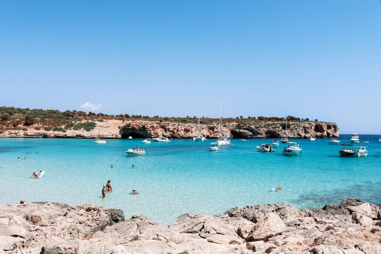 People swimming in turquoise blue water with boats in the background on the island of Mallorca