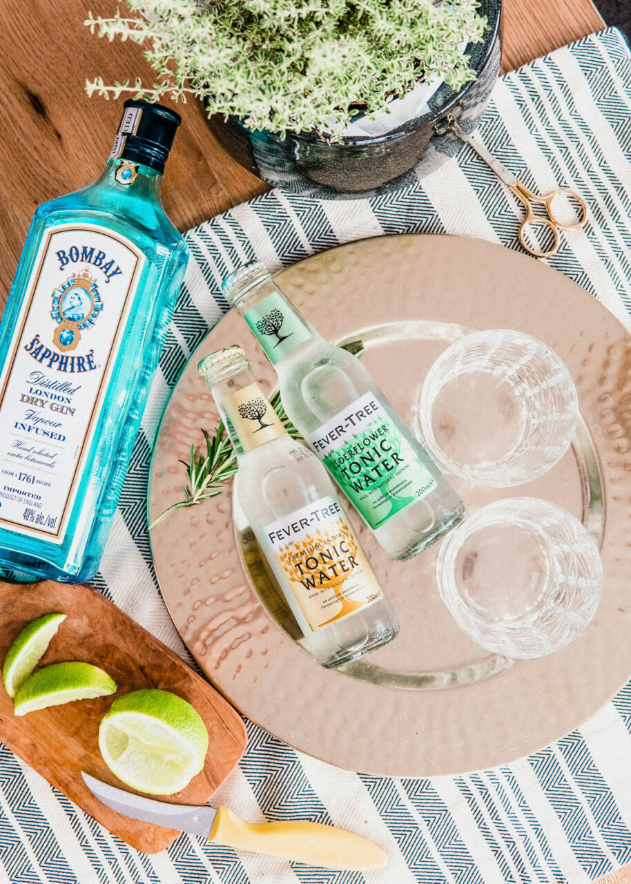 Bombay Sapphire on a table with bottles of Fever-Tree tonic water and limes