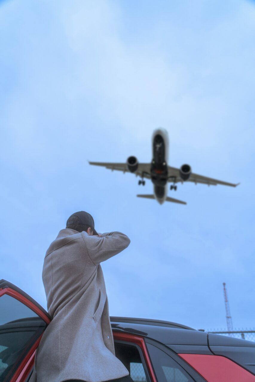 Man leaning out of a red car looking at an airplane