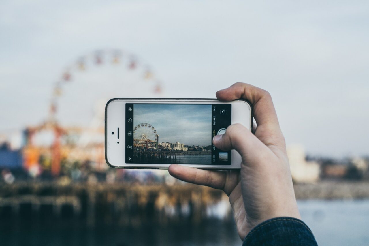 Hand holding a white iPhone taking a photo of a ferris wheel