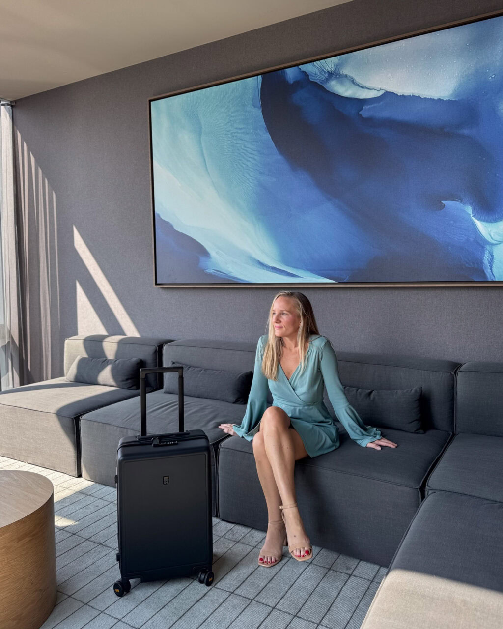 Woman sitting on a sofa in front of a blue painting with the Level8 Black carry on bag
