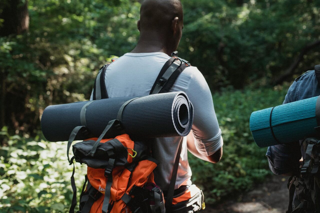 Black man walking through a forest with backpack and camping mat