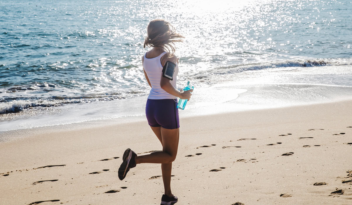 Woman jogging on sunny beach with water bottle